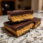 Three stacked squares of rich buckeye fudge showing a thick peanut butter center and dark chocolate topping.