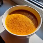 Close-up of vibrant orange butternut squash soup, topped with spices, served in a white bowl.