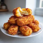 A stack of golden brown, crispy potato croquettes with one broken open showing a dramatic cheese pull.