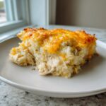 A generous serving of creamy chicken cauliflower rice casserole topped with melted, golden cheddar cheese.
