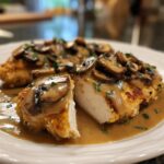 Close-up of a sliced chicken marsala breast showing juicy white meat covered in rich mushroom sauce and fresh parsley.