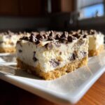 A close-up of a creamy chocolate chip cheesecake bar slice showing the graham cracker crust and mini chocolate chips.