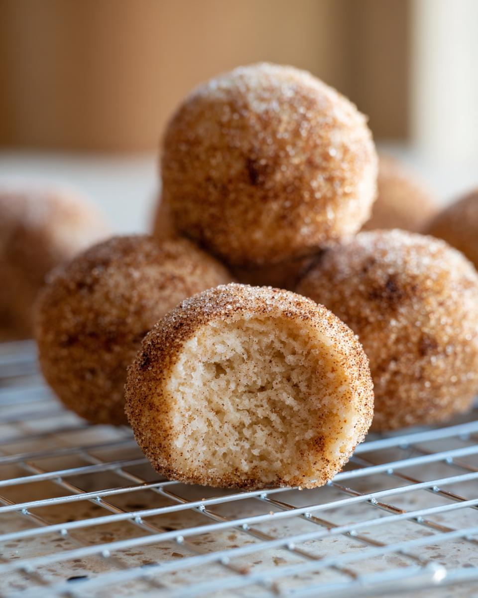 A close-up of several soft cinnamon sugar snowball cookies, with one cookie broken open to show the fluffy interior.