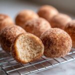 A close-up of soft cinnamon sugar snowball cookies cooling on a wire rack, one cookie is broken open showing the texture.