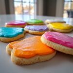 Close-up of several sugar cookies topped with brightly colored sugar cookie icing that hardens in shades of orange, pink, blue, and purple.