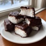 A stack of homemade cool whip candy squares coated in dark chocolate, with one piece bitten into.