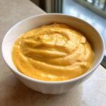 Close-up of a thick, creamy, bright orange beer cheese dip served in a white bowl.