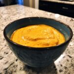 A close-up of thick, creamy orange cottage cheese queso served in a textured blue bowl on a granite countertop.