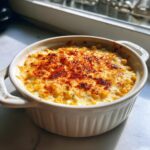 Close-up of a creamy, baked elote dip topped with browned cheese and paprika in a white serving dish.