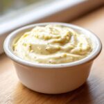 Close-up of thick, creamy homemade garlic aioli speckled with herbs and spices in a small white bowl.