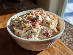 A close-up of a creamy, chunky hoagie dip filled with meat and vegetables served in a white bowl.
