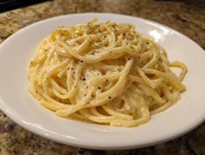 A close-up of creamy, cheesy parmesan pasta tossed with black pepper, served in a white bowl.