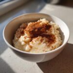 A close-up of creamy rice pudding recipe served in a white bowl, generously dusted with ground cinnamon.