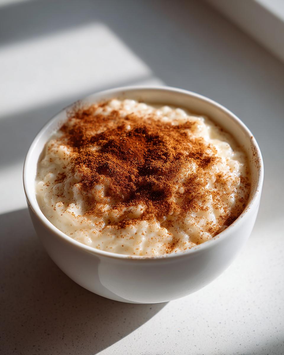 A close-up of a white bowl filled with creamy rice pudding recipe, generously dusted with cinnamon.