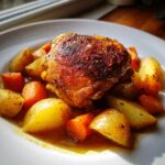A perfectly seared piece of braised chicken thighs served over roasted potatoes and carrots in a savory sauce.