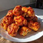 A pile of crispy, bright orange buffalo cauliflower bites coated in spicy sauce, served on a white plate.