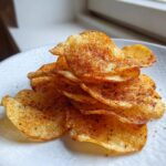 A stack of golden, homemade potato chips seasoned with dark spices, highlighting the crunch.