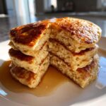 Close-up of a stack of fluffy coconut flour pancakes cut in half, drizzled with syrup.