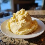 A large, fluffy mound of creamy, yellow mashed potatoes served on a white plate.