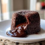A single, rich chocolate lava cake with molten chocolate oozing out onto a white plate.