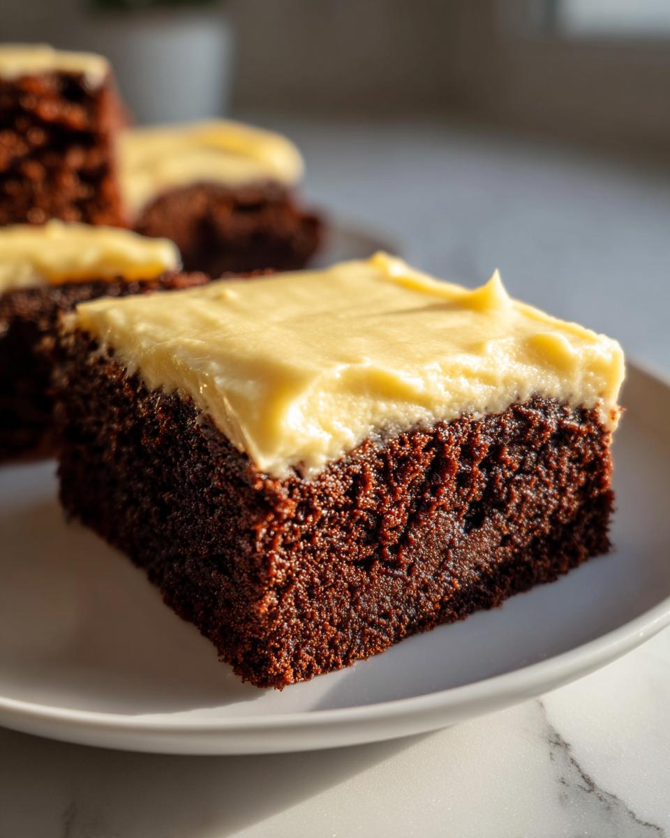 A close-up of a rich, dark chocolate gingerbread brownies square topped with thick, creamy yellow frosting.