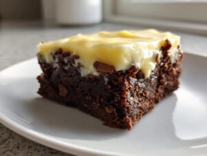 Close-up of a rich, fudgy gingerbread brownie square topped with thick, pale yellow frosting.
