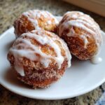 Close-up of three golden brown baked apple fritters coated in cinnamon sugar and drizzled with white glaze.