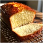 A golden brown loaf of homemade beer bread, partially sliced, resting on a cooling rack.