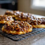 Close-up of gooey pecan pie cookies topped with caramelized pecans cooling on a black wire rack.