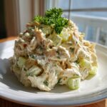 A tall serving of creamy greek yogurt chicken salad mixed with celery chunks and topped with fresh parsley.