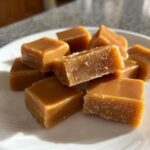 Close-up of several chewy cubes of homemade caramel sprinkled with salt on a white plate.