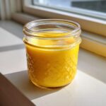 A vibrant, creamy yellow homemade salad dressing stored in a small, textured glass jar.