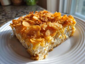 A square slice of hot chicken salad casserole featuring a creamy interior and a golden, crunchy cornflake topping.