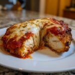 A cross-section of keto chicken parmesan showing juicy white chicken breast, marinara sauce, and gooey melted mozzarella cheese.