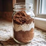 Close-up of layered dry ingredients for hot cocoa mix in a clear mason jar.