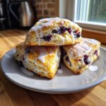 Three freshly baked lemon blueberry scones stacked on a plate, drizzled with white lemon glaze.