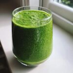 Close-up of a vibrant green matcha chia pudding smoothie texture in a clear glass, set by a window.