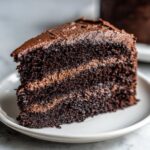 Close-up of a moist, dark slice of chocolate cake with rich chocolate frosting layers.