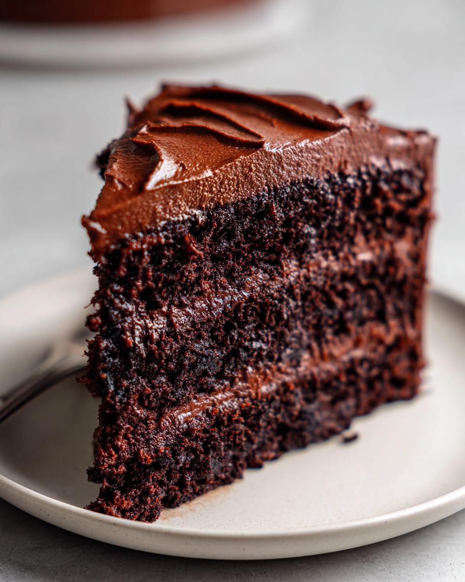 Close-up of a moist slice of dark chocolate cake layered with rich chocolate frosting.