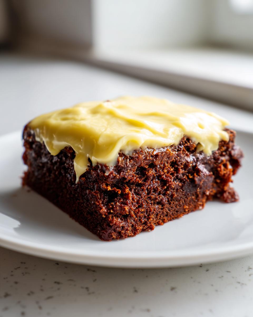 Close-up of a rich, dark gingerbread brownie square topped with thick, pale yellow frosting.