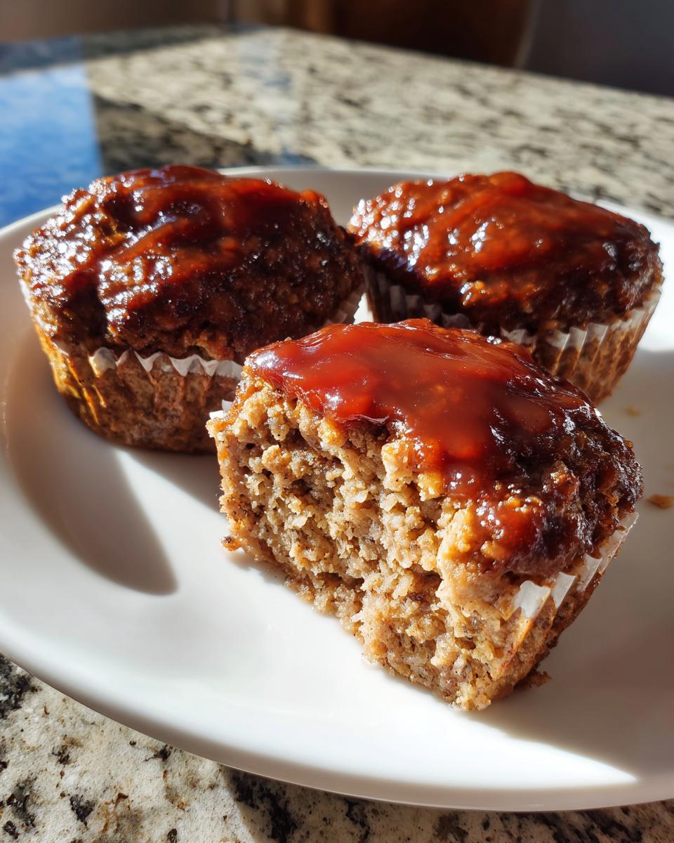 Three individual mini meatloaf portions topped with a shiny glaze, one cut open to show the texture.