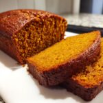 Close-up of a loaf of moist pumpkin bread with two thick slices cut and resting in front.