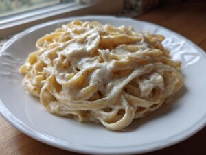 A close-up of fettuccine pasta generously coated in creamy Olive Garden Alfredo Sauce on a white plate.