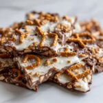 A stack of broken pieces of peanut butter pretzel bark topped with white chocolate, pretzels, and sea salt.