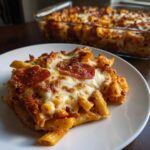 A generous serving of baked pizza pasta casserole topped with melted mozzarella and pepperoni slices on a white plate.