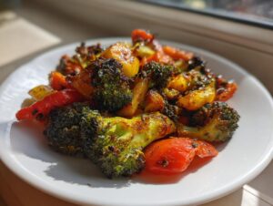 A close-up of perfectly roasted vegetables, including charred broccoli florets and bright red peppers, served on a white plate.
