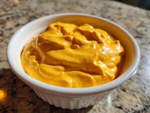 Close-up of thick, vibrant orange beer cheese dip served in a small white fluted bowl.