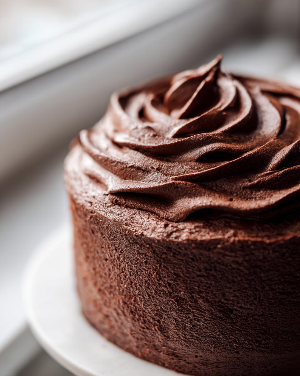 Close-up of a rich chocolate frosting piped in swirls atop a dark chocolate cake.