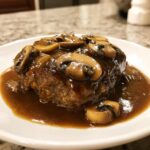 Close-up of a juicy Salisbury steak smothered in rich mushroom gravy on a white plate.