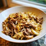 Close-up of tender, shredded pork and sauerkraut mixture served in a white bowl.